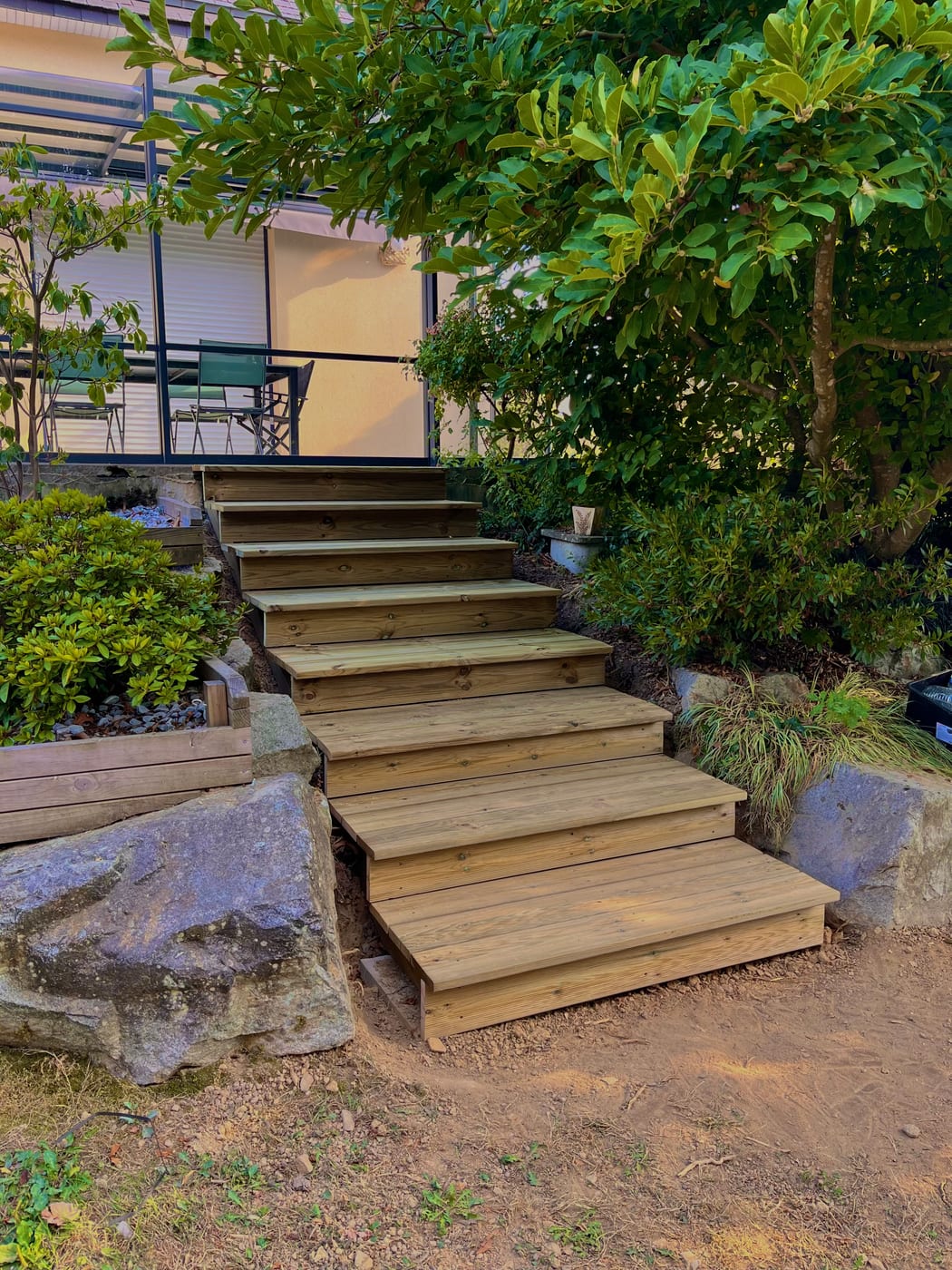 Après : escalier extérieur en bois reliant la terrasse au jardin, encadré de blocs de granit