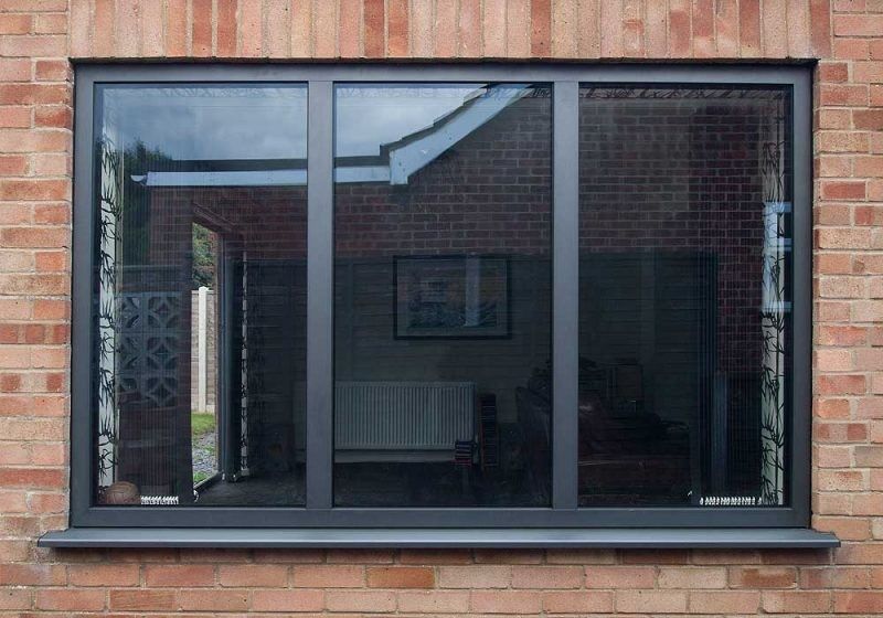Fenêtre fixe et ouvrants latéraux sur façade brique, vue du salon depuis l'extérieur