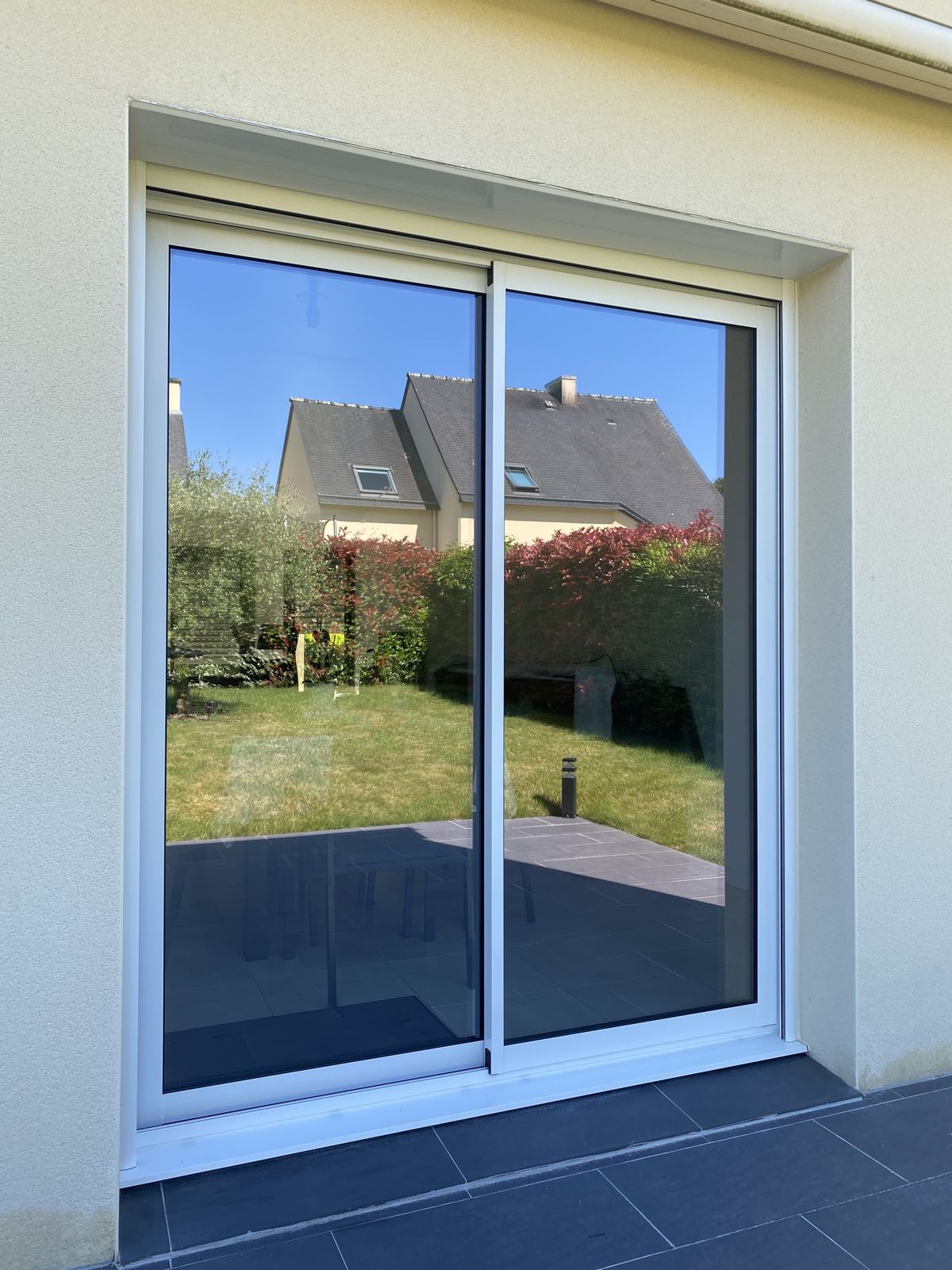 Fenêtre coulissante blanche vue de l'extérieur, avec reflet du jardin